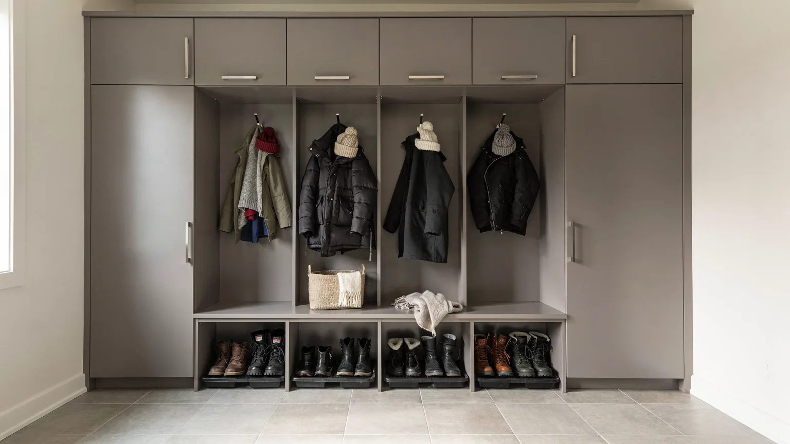 Vestiaire d'entrée sur mesure en mélamine gris chaud: banc, bottes sur plateau, casiers ouverts avec crochets et armoires jusqu'au plafond.