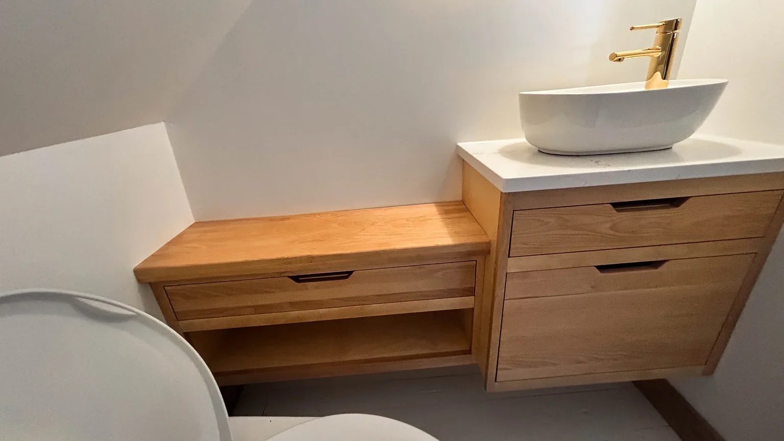 Vanité suspendue sur mesure en bois huilé, tiroirs à poignées encastrées et vasque posée sur un comptoir de quartz blanc.