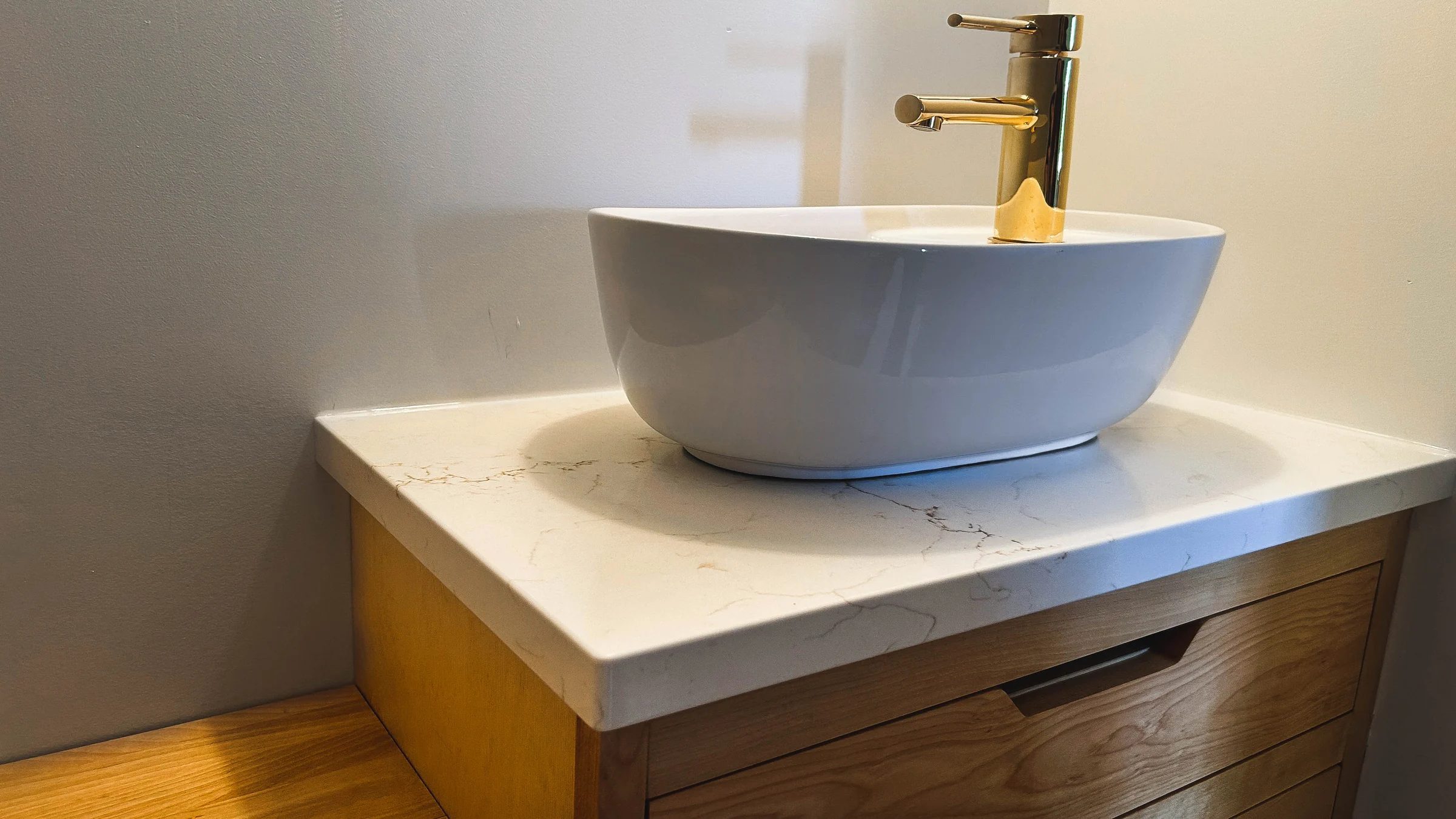 Lavabo vasque et robinet doré sur comptoir de quartz veiné, vanité en bois huilé