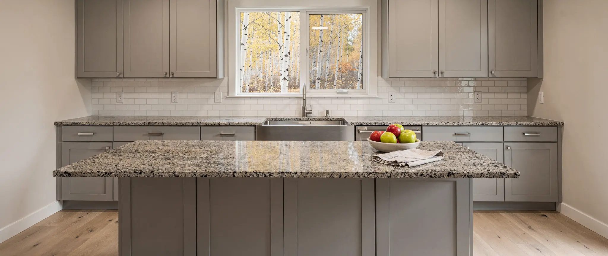 Reference illustration: polished granite countertop speckled black, grey and beige, on pale grey melamine cabinets, with a matching island