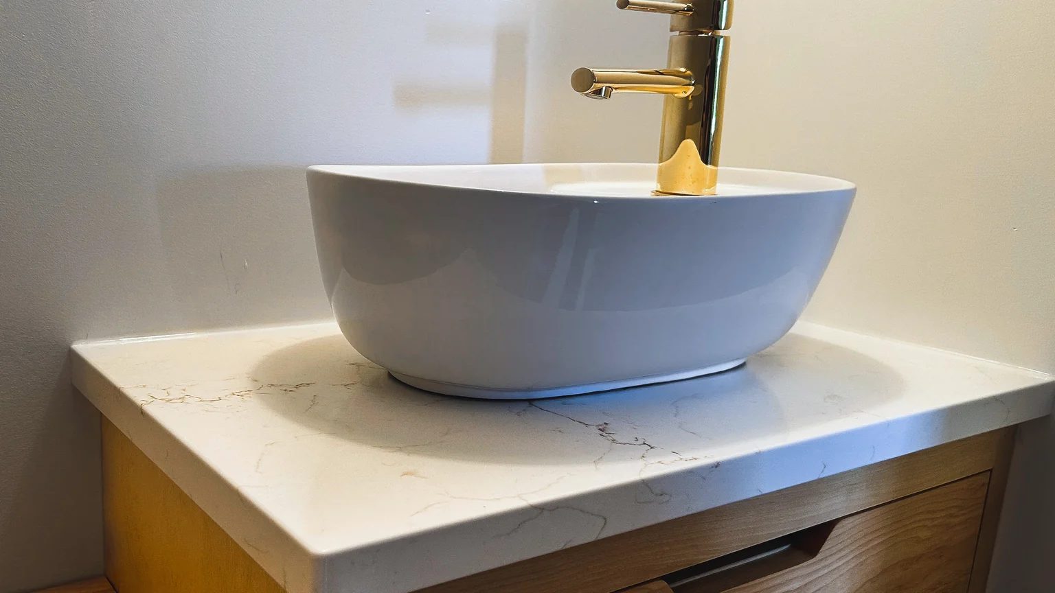 White veined quartz vanity top with an eased square edge, a vessel sink and a gold faucet.