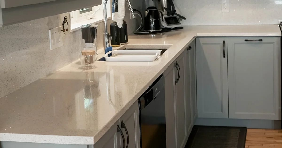 Light speckled quartz countertop with an undermount sink and a matching quartz backsplash, on grey Shaker cabinets.