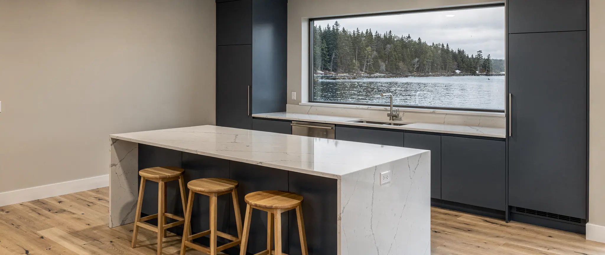 Reference illustration: kitchen island with a white quartz countertop veined in grey, on slate-blue melamine cabinets, in front of a window onto a bay