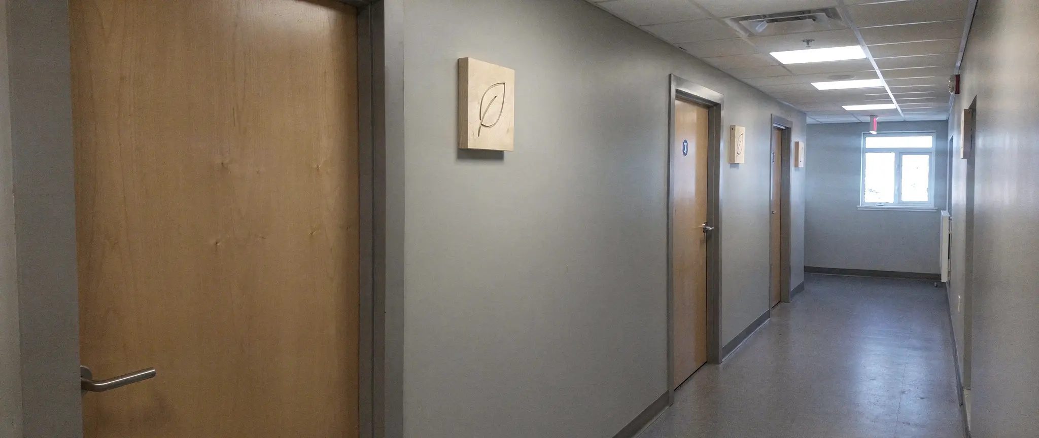 Reference illustration: engraved wood interior signage, small identical birch signs engraved with a leaf, beside the doors of an office corridor